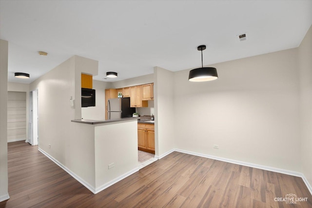 kitchen with light brown cabinetry, decorative light fixtures, light hardwood / wood-style floors, and stainless steel refrigerator