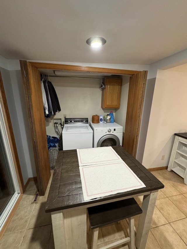 clothes washing area featuring separate washer and dryer, light tile patterned floors, and cabinets