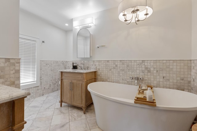 bathroom with an inviting chandelier, vanity, a washtub, and tile walls