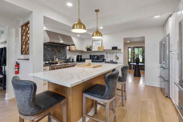 kitchen featuring pendant lighting, white cabinetry, a center island, exhaust hood, and light stone countertops