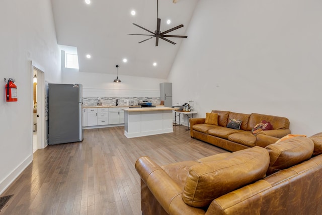 living room with ceiling fan, light hardwood / wood-style flooring, and a high ceiling