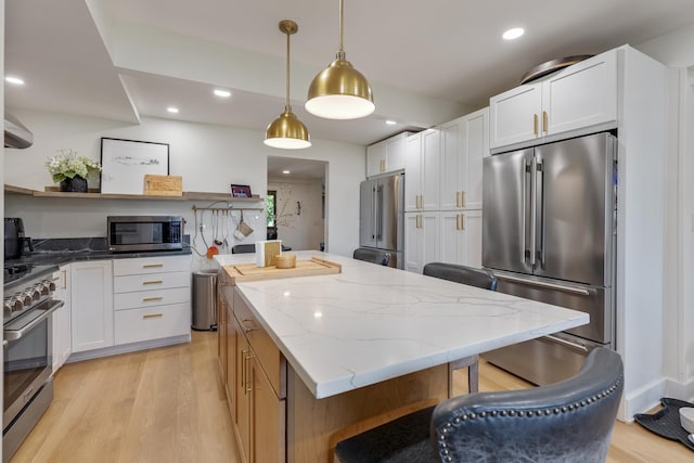 kitchen featuring high end appliances, light stone counters, decorative light fixtures, a center island, and white cabinets