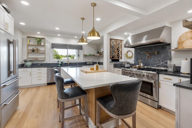 kitchen featuring high end appliances, white cabinetry, light hardwood / wood-style flooring, a kitchen island, and wall chimney range hood