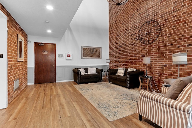 living room with a high ceiling, brick wall, and light hardwood / wood-style floors