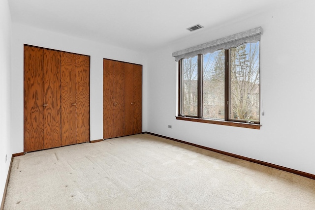 unfurnished bedroom featuring light carpet and two closets