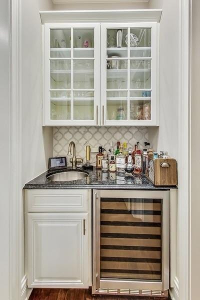 bar with sink, dark stone countertops, beverage cooler, and backsplash