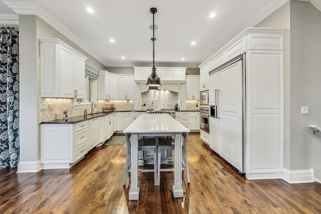 kitchen featuring pendant lighting, sink, white cabinetry, a kitchen breakfast bar, and built in appliances