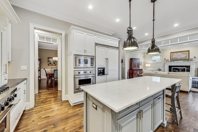 kitchen with decorative light fixtures, white cabinetry, a center island, built in appliances, and crown molding