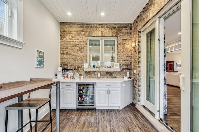 bar with wine cooler, white cabinetry, dark wood-type flooring, and brick wall