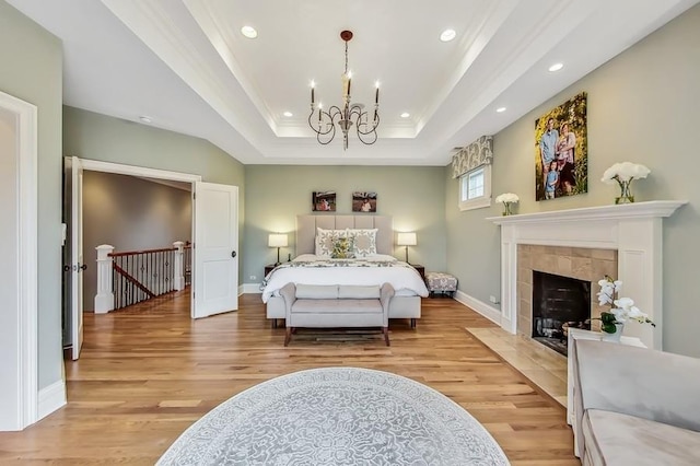 bedroom featuring a notable chandelier, a tray ceiling, a fireplace, ornamental molding, and light hardwood / wood-style floors