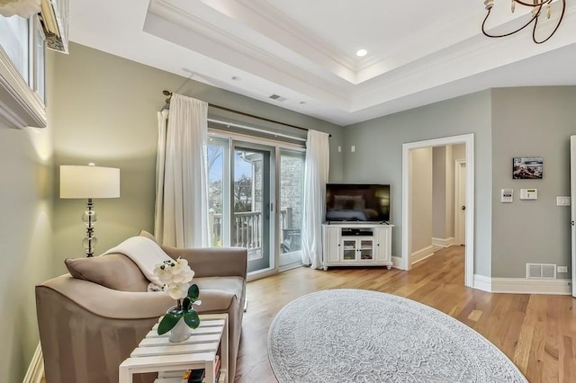 living room featuring crown molding, a tray ceiling, and light hardwood / wood-style floors