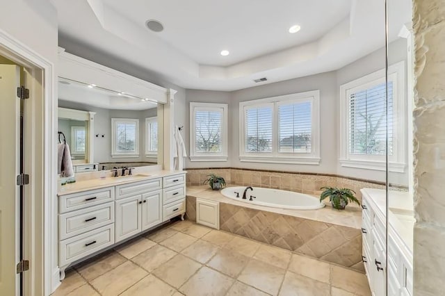 bathroom with vanity, tiled bath, a raised ceiling, and plenty of natural light