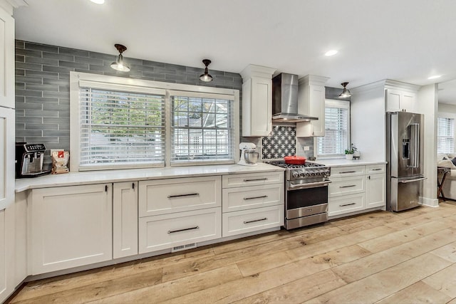 kitchen featuring premium appliances, light hardwood / wood-style floors, white cabinets, and wall chimney exhaust hood