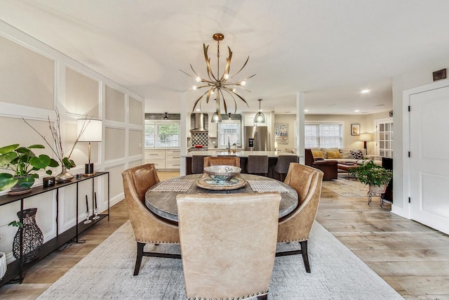 dining room with sink, a healthy amount of sunlight, an inviting chandelier, and light wood-type flooring