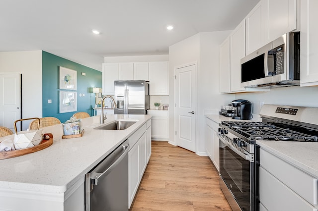 kitchen with sink, white cabinetry, stainless steel appliances, light stone countertops, and a center island with sink