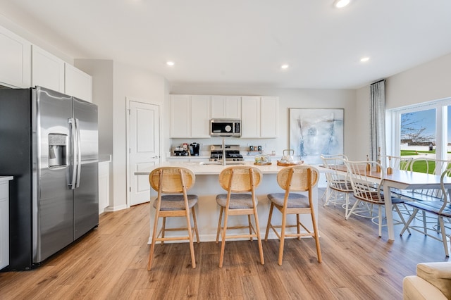 kitchen with a breakfast bar area, stainless steel appliances, white cabinets, and a center island with sink