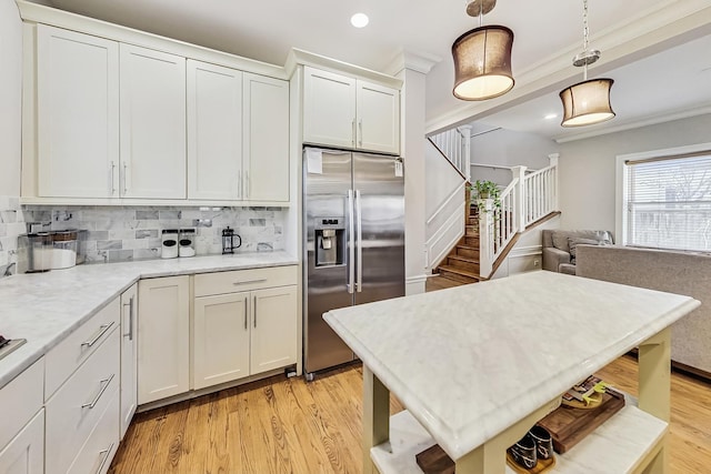 kitchen featuring crown molding, stainless steel fridge with ice dispenser, hanging light fixtures, white cabinets, and backsplash