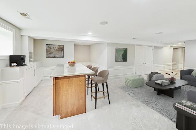 kitchen featuring white cabinetry, a center island, light colored carpet, and a kitchen bar