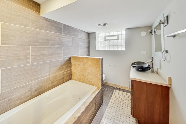 bathroom with a relaxing tiled tub, vanity, and toilet