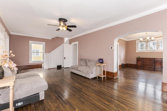 living room with arched walkways, ceiling fan with notable chandelier, baseboards, ornamental molding, and dark wood-style floors