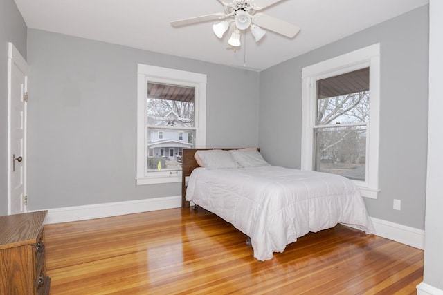 bedroom with multiple windows, ceiling fan, baseboards, and wood finished floors