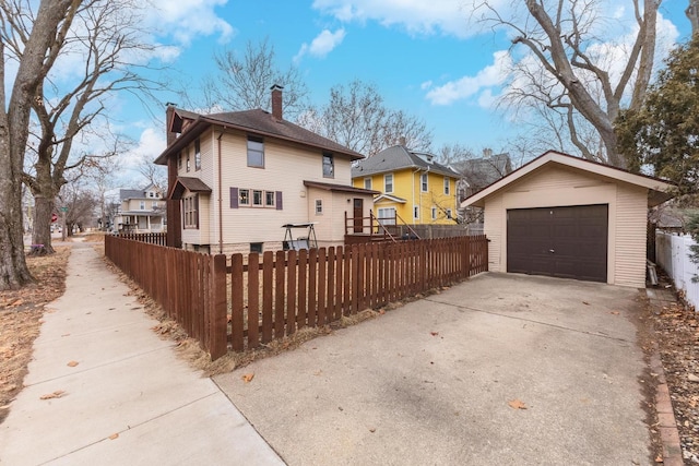 view of front of property with a fenced front yard, a chimney, a garage, driveway, and an outdoor structure