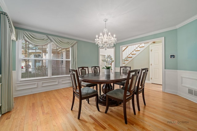 dining space featuring wainscoting, crown molding, a chandelier, and light wood-style floors