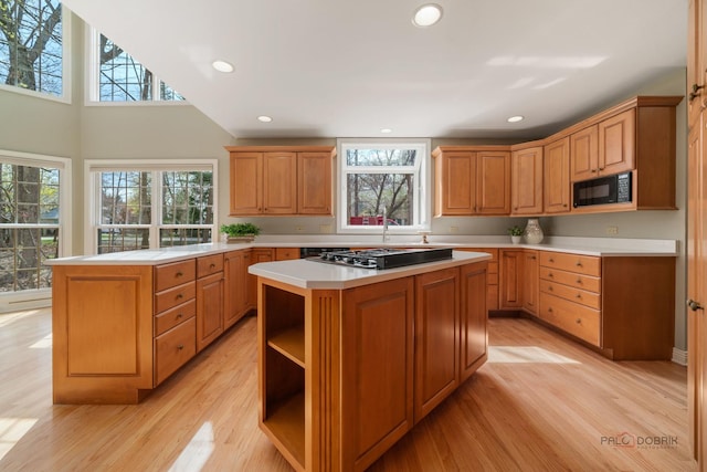 kitchen with light wood-style floors, stainless steel gas stovetop, black microwave, light countertops, and a kitchen island