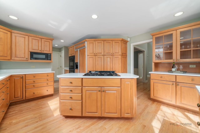 kitchen with black microwave, gas cooktop, light wood-style floors, glass insert cabinets, and light countertops
