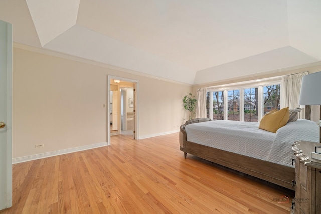 bedroom featuring vaulted ceiling, ensuite bathroom, light wood-type flooring, a tray ceiling, and baseboards
