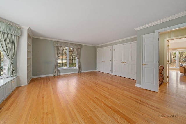 unfurnished bedroom with two closets, crown molding, multiple windows, and light wood-style flooring