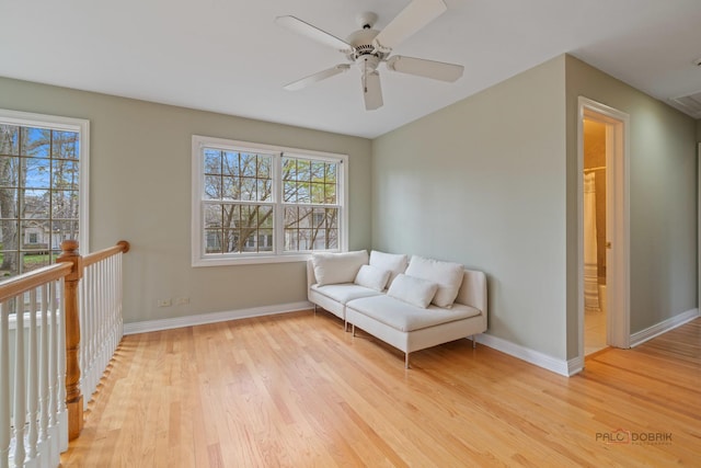 living area with light wood-type flooring, a ceiling fan, and baseboards