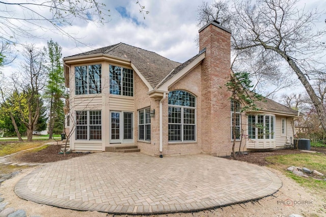 rear view of house with brick siding, a patio, central AC, and a chimney