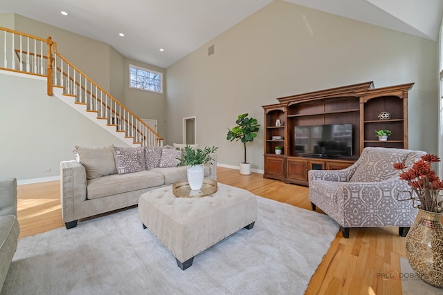 living room with recessed lighting, light wood-style flooring, high vaulted ceiling, and stairs