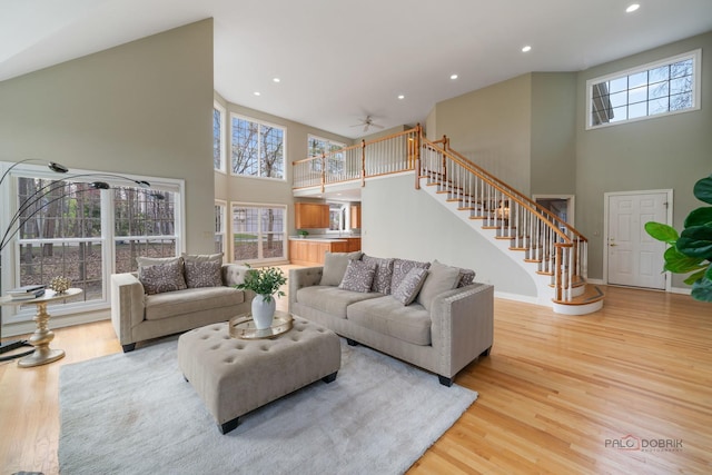 living area featuring stairway, ceiling fan, a high ceiling, and light wood-style floors