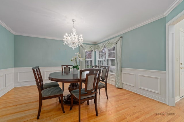 dining room featuring light wood-type flooring, ornamental molding, a notable chandelier, and wainscoting