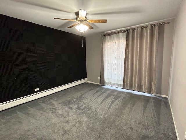 carpeted spare room with ceiling fan and a baseboard radiator