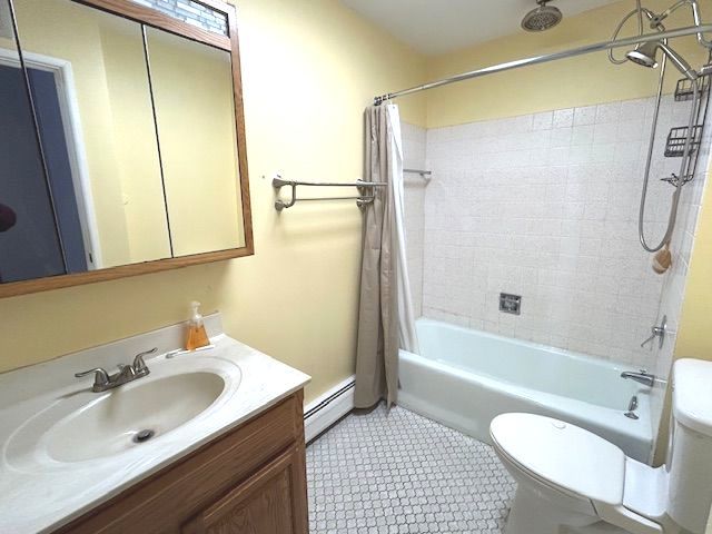 full bathroom with toilet, baseboard heating, vanity, shower / bath combo with shower curtain, and tile patterned flooring