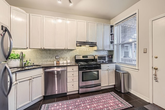 kitchen featuring decorative backsplash, stainless steel appliances, dark stone counters, and white cabinets