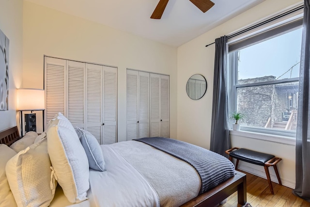 bedroom with two closets, wood-type flooring, and ceiling fan