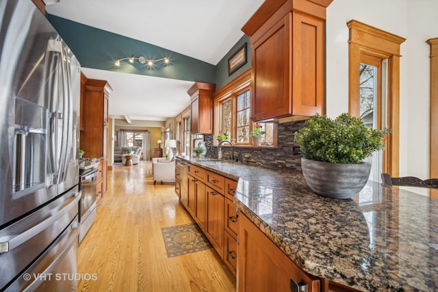 kitchen with sink, light hardwood / wood-style flooring, dark stone countertops, stainless steel appliances, and decorative backsplash