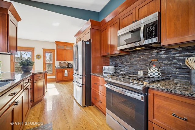 kitchen with tasteful backsplash, light hardwood / wood-style floors, dark stone counters, and appliances with stainless steel finishes