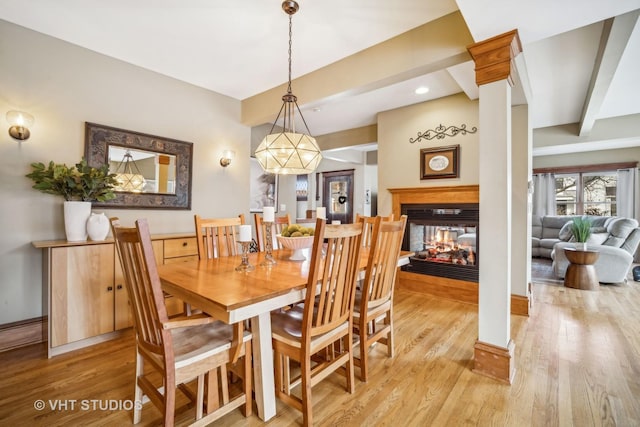 dining space with ornate columns, a multi sided fireplace, beam ceiling, and light wood-type flooring