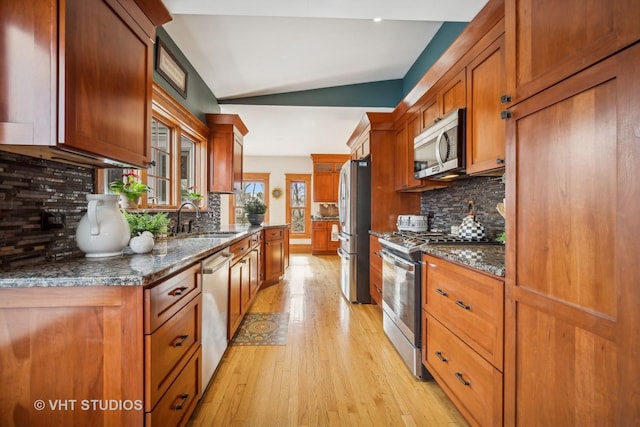 kitchen with appliances with stainless steel finishes, lofted ceiling, sink, decorative backsplash, and light hardwood / wood-style floors