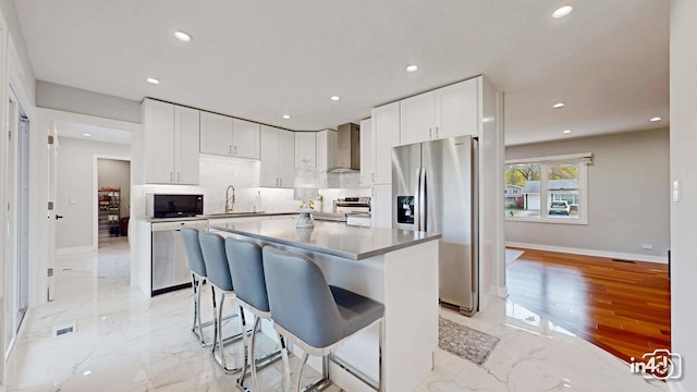 kitchen with a kitchen island, appliances with stainless steel finishes, white cabinetry, sink, and wall chimney range hood