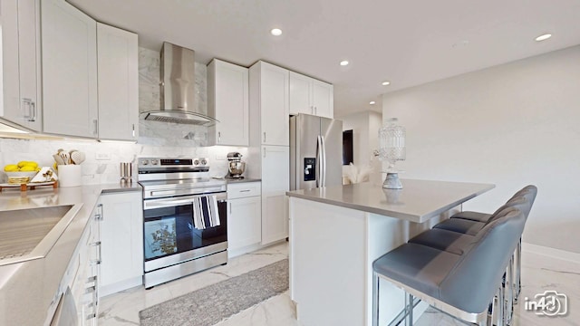 kitchen featuring wall chimney exhaust hood, white cabinetry, a center island, appliances with stainless steel finishes, and a kitchen breakfast bar