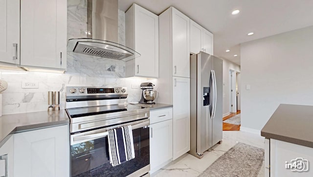 kitchen featuring white cabinetry, appliances with stainless steel finishes, tasteful backsplash, and wall chimney range hood