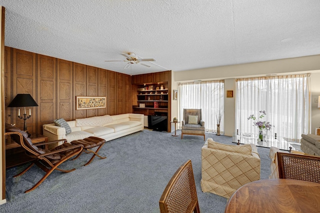 carpeted living room featuring ceiling fan, a textured ceiling, and wood walls