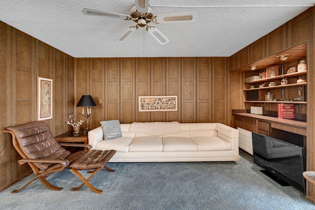 living room featuring ceiling fan, wooden walls, a textured ceiling, and carpet flooring