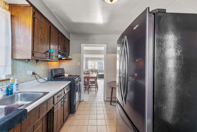 kitchen featuring sink, tasteful backsplash, light tile patterned floors, stainless steel fridge, and black gas stove